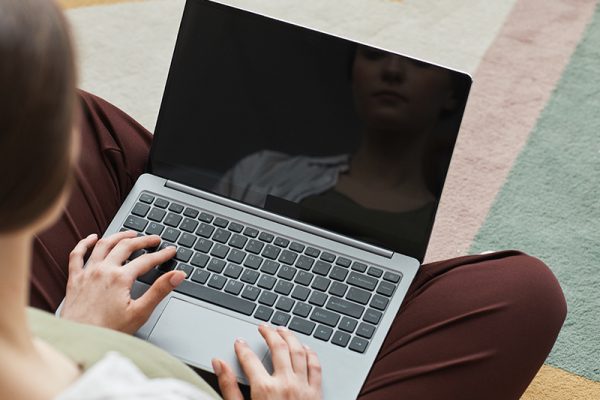 Rear view of young woman typing on laptop and working online while sitting in the room