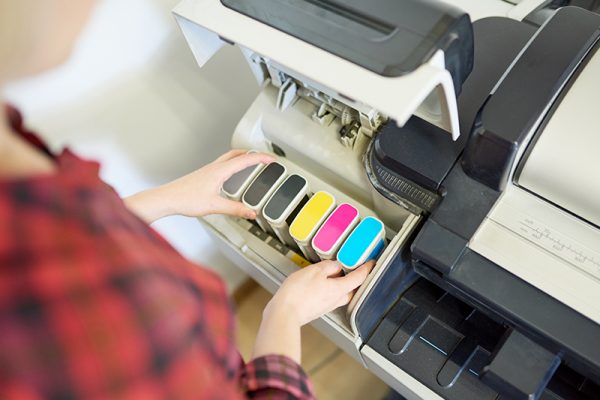 From above shot of anonymous woman putting set of ink into plotter in printing office.